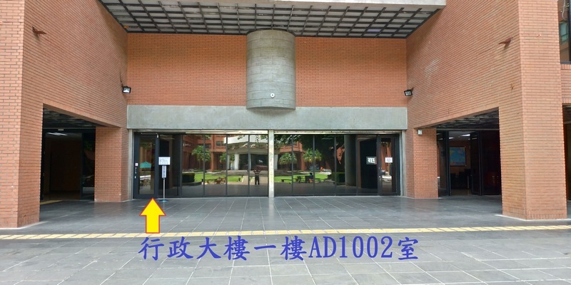 行政大樓後方左側門口，黃色箭頭指向入口，下方標示「行政大樓一樓 AD1002 室」